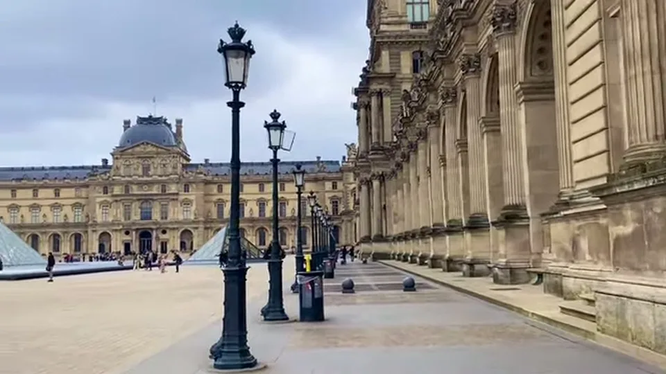 Louvre courtyard with colonnade, lampposts and glass pyramid under a gray winter sky